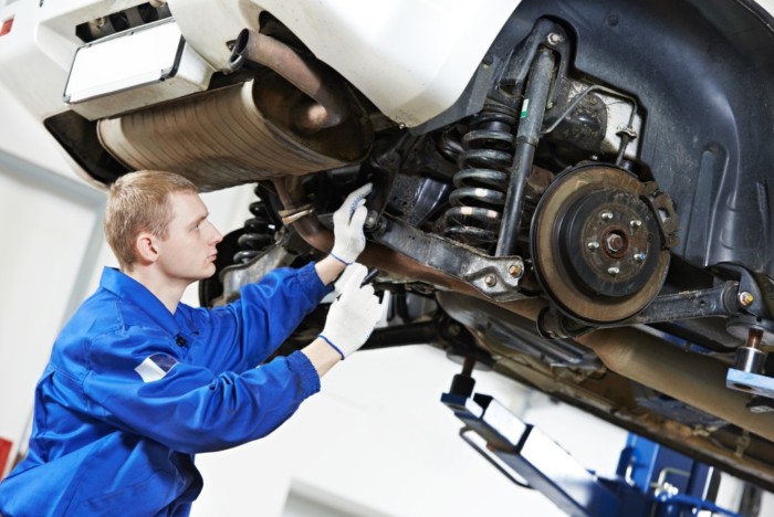 car mechanic inspecting car wheel and suspension detail of lifted automobile at repair service station